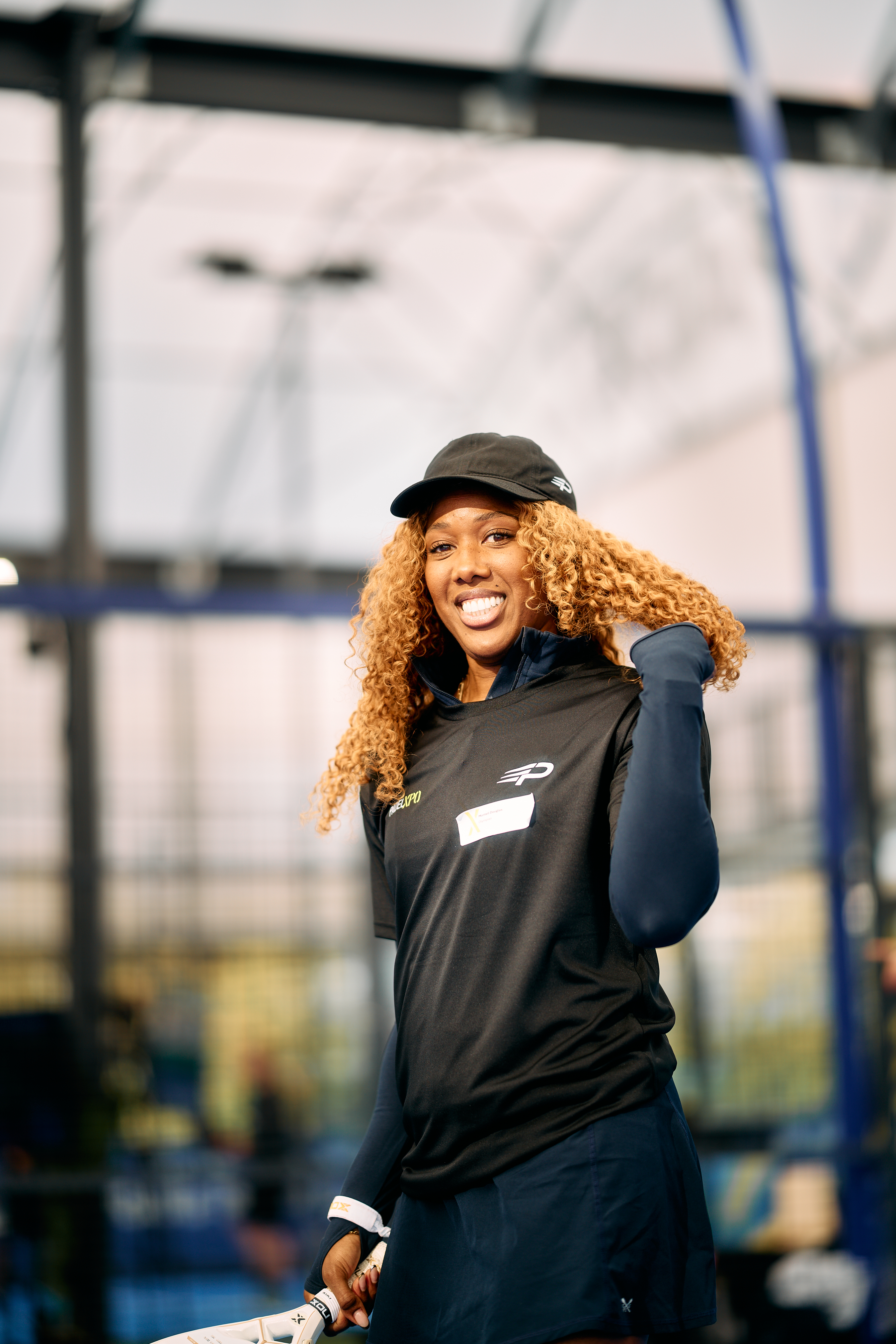 Smiling player in a black cap holding a padel racket