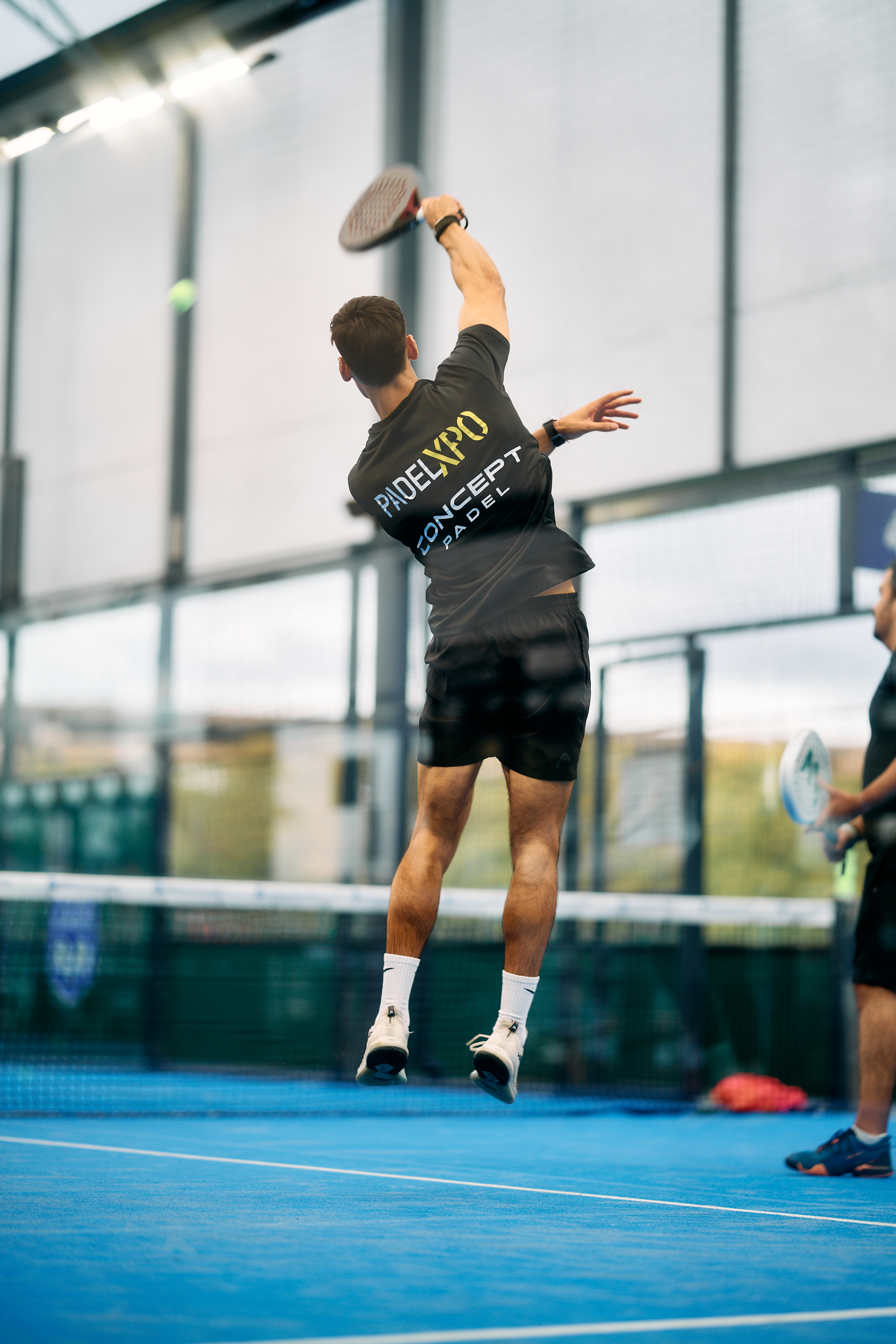 Player in a PadelXPO shirt jumping to hit an overhead smash