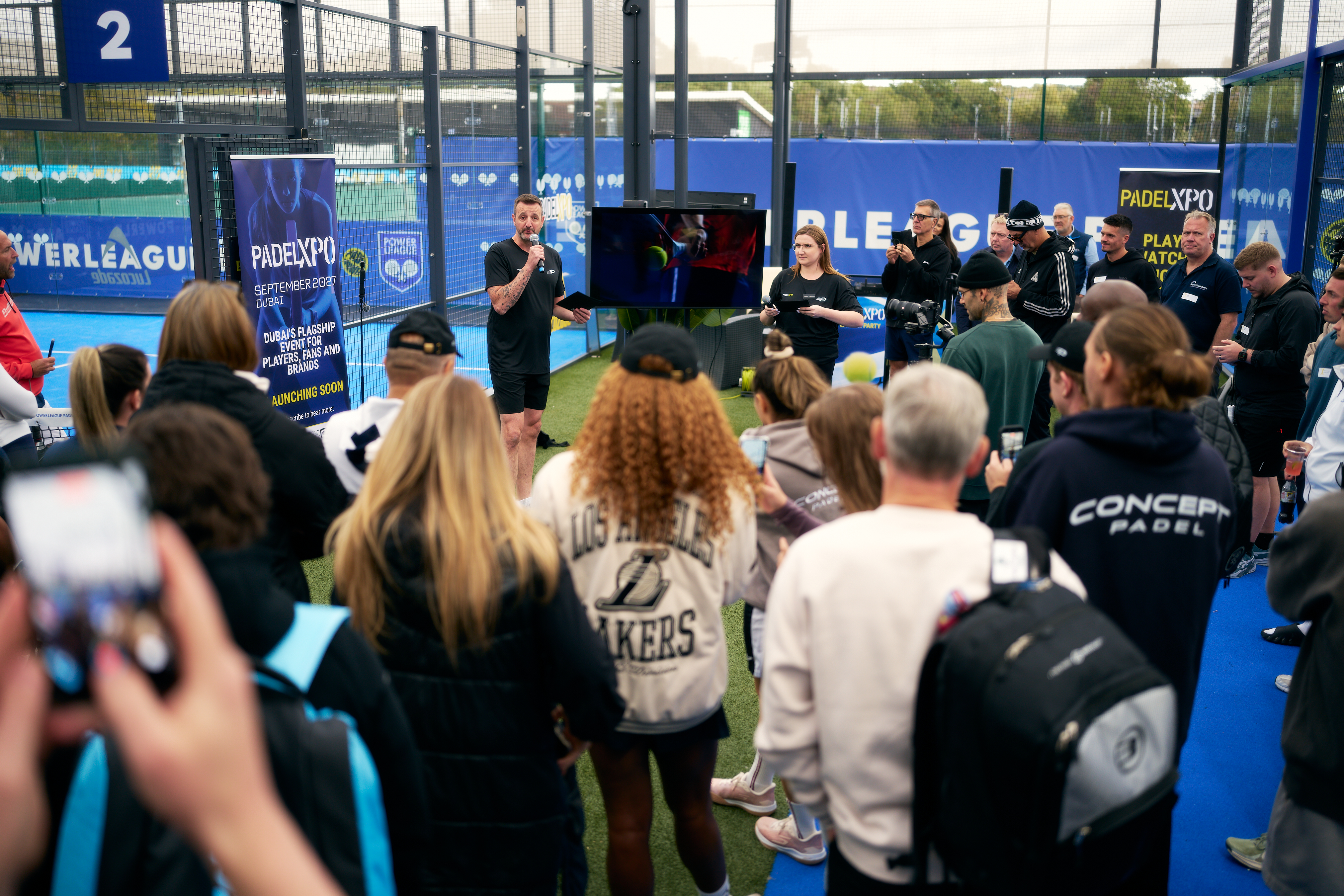 Speaker addressing a crowd of guests beside a PadelXPO banner